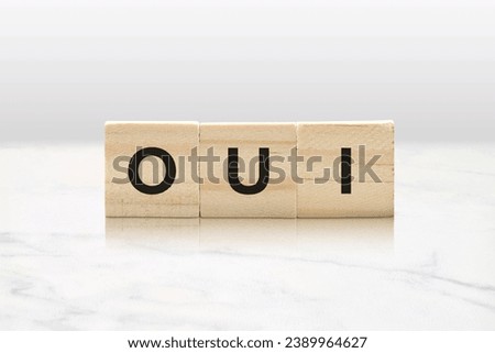 Three wooden tiles spelling OUI against a classy white marble background.