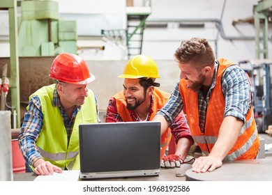 Three workers in factory together in front of laptop computer looking at email with order