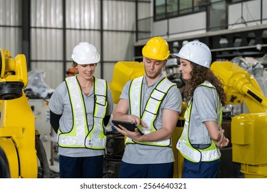 Three workers in safety gear review data on a tablet while surrounded by robotic machinery in a modern factory setting during daytime. - Powered by Shutterstock