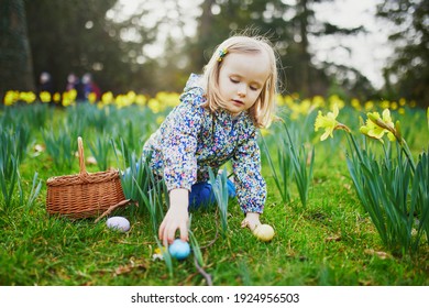 Three year old girl playing egg hunt on Easter. Child sitting on the grass with many narcissi and gathering colorful eggs in basket. Little kid celebrating Easter outdoors in park or forest - Powered by Shutterstock