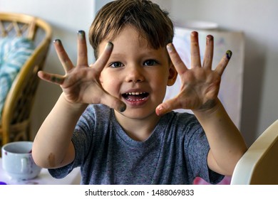 Three Years Boy With Finger Paint Looking At Camera. Toddler Sitting At The Table And Painting For School. Happy Smiling Kid Enjoying Arts And Crafts Painting With Hands. Boy Is Preparing For School. 