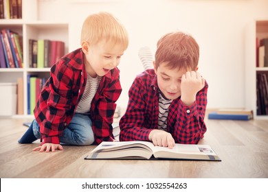 Three years old child and his older brother sitting among books at home. Curious boys reading in white room