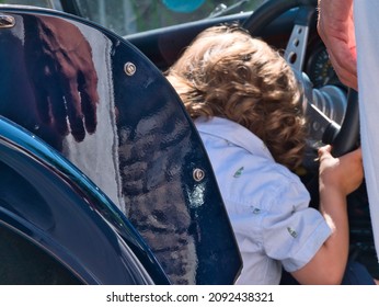 A Three Years Old Toddler Enjoys Playing Like He Is Driving A British Classic Car