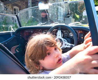 A Three Years Old Toddler Enjoys Playing Like He Is Driving A British Classic Car