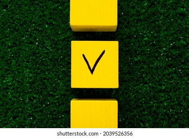 Three Yellow Cubes With A Tick On One On Grass. Concept Of Choosing A Better Option, Creating Checklists, Elections And Sports Betting