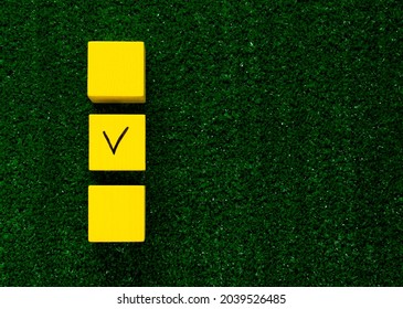 Three Yellow Cubes With A Tick On One On Grass. Copy Space. Concept Of Choosing A Better Option, Creating Checklists, Elections And Sports Betting