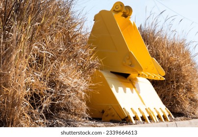 Three yellow frontend loader buckets stacked on top of each other in the dry grass.