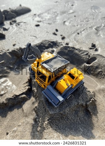Three yellow Kids toys laying on a sand pile in a beach. Yellow Bulldozer, yellow tractor on a sand in Bali, Indonesia.