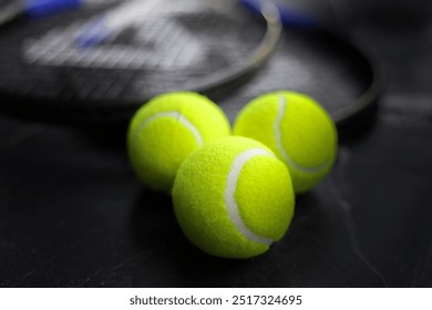 Three yellow tennis balls are lying in a wedge, the focus is on the front of the balls, tennis rackets are visible from behind in disfocus on a dark background, side view. High quality photo - Powered by Shutterstock