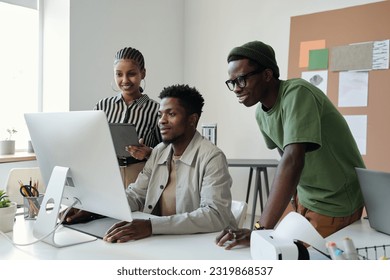 Three young African American graphic designers looking at computer screen at working meeting while one of them drawing sketch - Powered by Shutterstock