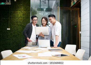 three young asian entrepreneurs meeting in office discussing business using laptop computer