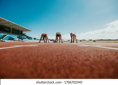 Three young athletes at starting position ready to start a race. Sports women ready for race on racetrack. - Powered by Shutterstock