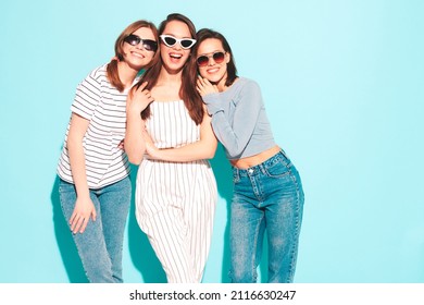 Three young beautiful smiling hipster female in trendy summer clothes.Sexy carefree women posing near blue wall in studio.Positive models in sunglasses. Cheerful and happy