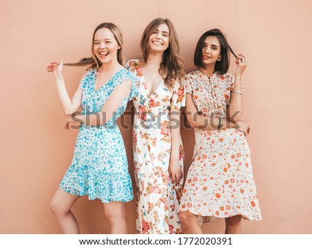 Three young beautiful smiling hipster girls in trendy summer sundress.Sexy carefree women posing near wall on the street background. Positive models having fun and hugging.Walking after shopping
