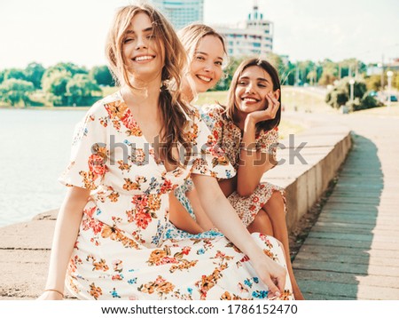 Three young beautiful smiling hipster girls in trendy summer sundress.Sexy carefree women posing on the street background. Positive models having fun and hugging. Sitting after shopping