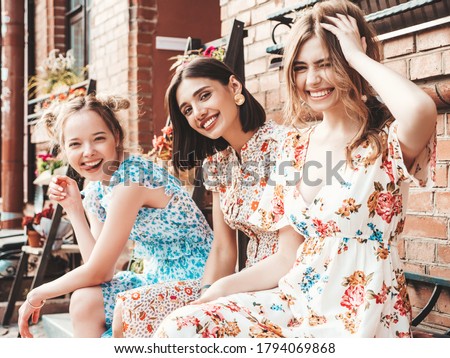 Three young beautiful smiling hipster girls in trendy summer sundress.Sexy carefree women posing on the street background.Models having fun and hugging. Sitting on the bench after shopping