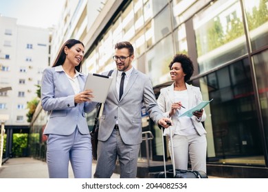 Three young business people talking to each other while walking outdoors with suitcase. - Powered by Shutterstock