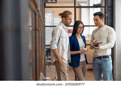 Three young business professionals standing together and discussing over business report in office hallway. Office colleagues checking a business document on the tablet in coworking - Powered by Shutterstock