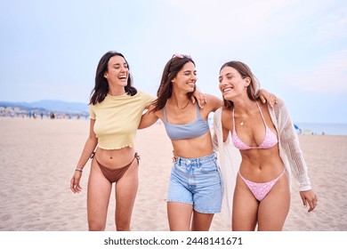 Three young Caucasian beautiful women friends embracing in swimwear posing cheerful on beach holidays. Group of gen z female hugging standing smiling on sunny summer time - Powered by Shutterstock