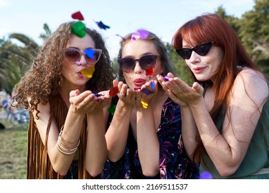 Three Young Caucasian Women Blowing Confetti Towards Camera On Music Festival