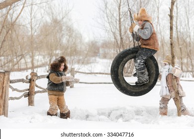 Three Young Children Playing And Swinging On The Wheel, Hanging In The Backyard Of The House, A Warm Winter Day