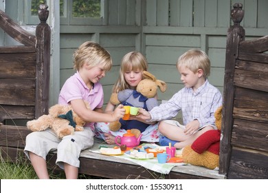 Three young children in shed playing tea and smiling