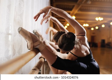 three young cute ballerinas perform exercises on a choreographic machine or barre on the background of a ballet class