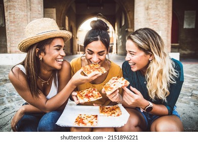 Three young female friends eating pizza sitting outside - Happy women enjoying street food in the city - Italian food culture and european holidays concept - Powered by Shutterstock