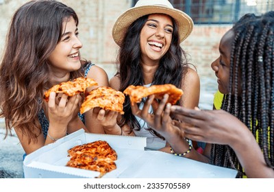 Three young female friends eating pizza sitting outside - Happy women enjoying street food in the city - Italian food culture and european holidays concept - Powered by Shutterstock