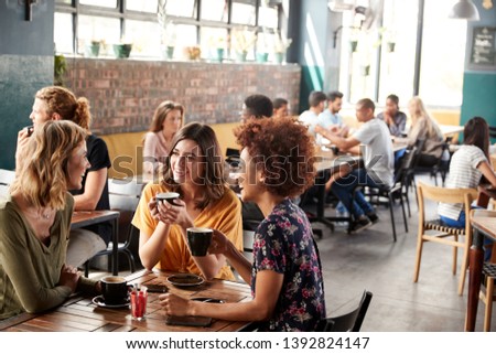 Three Young Female Friends Meeting Sit At Table In Coffee Shop And Talk