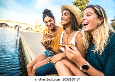 Three young female friends sitting outdoor and eating pizza - Happy women having fun enjoying a day out on city street - Happy lifestyle concept