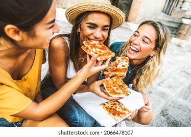 Three young female friends sitting outdoor and eating pizza - Happy women having fun enjoying a day out on city street - Happy lifestyle concept - Powered by Shutterstock