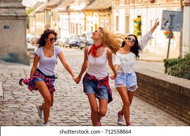 Three Young Female Friends Walking In City Street Laughing And Having Fun.