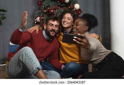 Three Young Friends Celebrate Christmas And New Year's Eve Together By Joking And Taking Selfies With A Smartphone Goofy And Making Funny Facial Expressions In Front Of The Christmas Tree