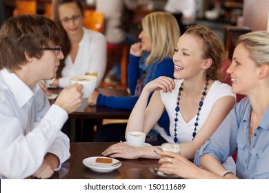 Three young friends having coffee together in a cafe seated around a small table chatting and smiling