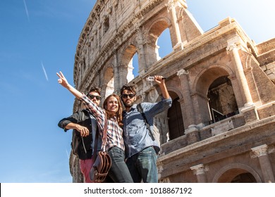 Three young friends tourists posing for funny pictures in front of colosseum in rome. Blue sky and lens flare on sunny day. - Powered by Shutterstock