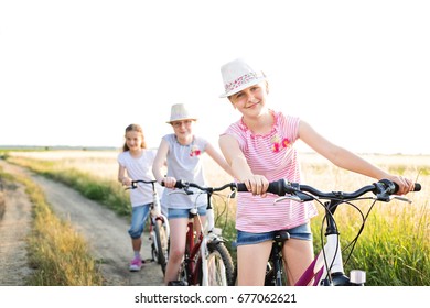 Three young girls on a bicycles in the field on sunny summer day