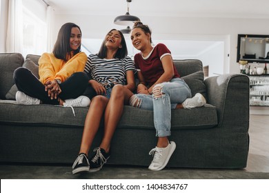 Three Young Girls Sitting Together On A Couch In Living Room And Laughing. Teenage Girls Having Fun Sitting Together And Talking At A Sleepover.