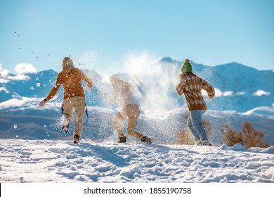 Three Young Happy Girls Friends Are Having Fun In Snow Fight In Mountains. First Snow And Winter Vacations Concept