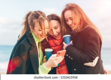 Three Young Happy Girls Watching Smartphone And Laughing - Group Of Friends Drinking Coffee To Go And Having Fun Together