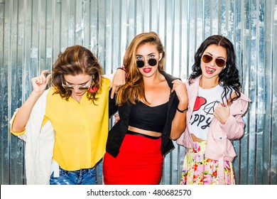 Three Young Happy Sexy Girl On A Background Of Metallic Wall, Bright, Fashionable Casual Wear, Fashion Accessories, Sunglasses, Best Friends Having Fun, Crazy, Long, Healthy Hair, Red Lips Urban Style