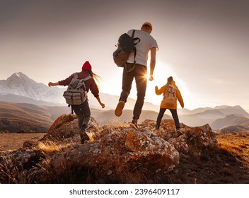 Three young hikers with small backpacks walks at sunset mountains. Weekend activities concept - Powered by Shutterstock