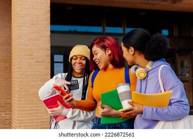 three young latina girls laughing and looking at the smartphone of one of them as they leave class at the university. - Shutterstock ID 2226872561