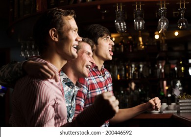 Three Young Men At Bar Watching Match And Shouting