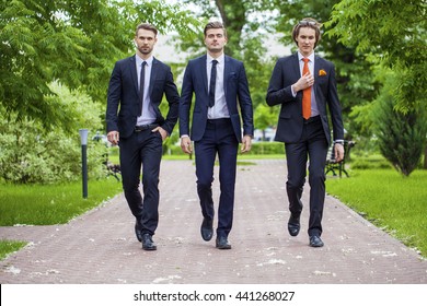 Three Young Men In Elegant Business Suits Walking In Summer Street, Outdoors