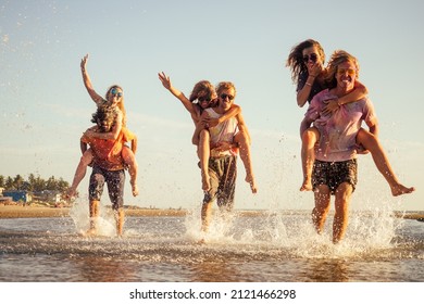 three young men giving their girlfriends piggyback rides at the beach in Goa India happy holi festival - Shutterstock ID 2121466298