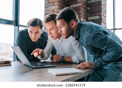 Three young men in an office, staring in amazement at their laptop screens. The work in front of them seems to have left them flabbergasted and bewildered.
