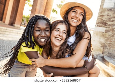 Three young multicultural women having fun together on city street - Happy female tourists enjoying summer vacation outside - Best friends hugging together - Friendship and life style concept - Powered by Shutterstock