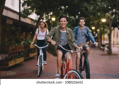 Three young people cycling down the street. Male and female friends on road with their bikes. - Shutterstock ID 1080226652
