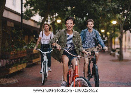 Three young people cycling down the street. Male and female friends on road with their bikes.